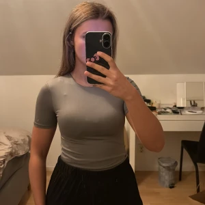 Grå tight kortärmad body - Säljer en grå, tight och kortärmad string body rund hals. Toppen är enkel och stilren, tillverkad i ett stretchigt syntetmaterial som sitter snyggt mot kroppen. Perfekt för dig som gillar en clean look och vill ha något som är lätt att matcha.