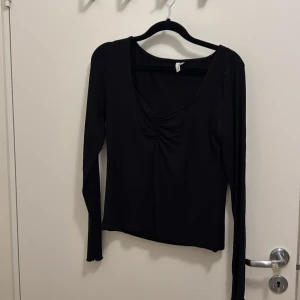 Svart långärmad topp från NLY Trend - Svart långärmad topp från NLY Trend med snygg v-ringning och rynkade detaljer framtill. Tillverkad i mjukt och stretchigt material som sitter skönt på kroppen. Perfekt att styla med jeans eller kjol för en clean look.