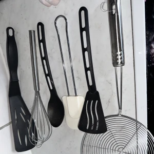 Köksredskap set – stekspade, visp, sked, tång, slickepott, hålslev - Diverse köksredskap säljes. Praktiskt set med sex köksredskap i plast och rostfritt stål. Innehåller stekspade, visp, sked, tång, slickepott och hålslev. Alla delar ser ut att vara i gott skick utan synligt slitage eller defekter. Perfekt för matlagning och bakning i hemmet.