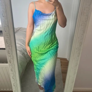 Färgglad långklänning från Zara 🩵 - Säljer en maxiklänning från Zara med tunna axelband och öppen rygg. Klänningen har ett snyggt färgskiftande mönster i blått och grönt. Materialet är mjukt och har en satinliknande känsla 💚