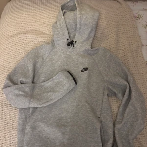 Grå Nike hoodie  - Snygg ljusgrå hoodie från Nike med svart logga på bröstet. Tröjan har huva med snörning och långa ärmar. Perfekt för chill dagar eller när du vill ha en sportig look. Mjuk och skön i bomullsblandning.
