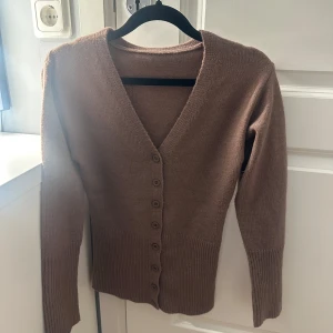 Brun kofta med v-ringning - Säljer en brun kofta med v-ringning och långa ärmar, strl XS. Den är figurnära och stickad i mjukt material, perfekt för lager-på-lager under höst och vinter.