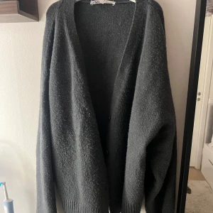 Mörkgrå oversized kofta från Zara - Mysig och oversized mörkgrå kofta från Zara med lång ärm och ribbade muddar. Koftan har en enkel design utan synliga knappar och är tillverkad i ett mjukt, stickat material som känns skönt mot huden. Perfekt för lager-på-lager under kyliga dagar.