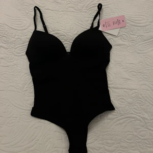 Svart body från H&M - Den populära bodyn från H&M. Kan tänka mig att gå ner i pris vid snabb affär💕🔥❤️. Slutsåld överallt. Justerbara axelband och vadderade kupor. Snygg och tight passform som framhäver siluetten. Ny med tag kvar!