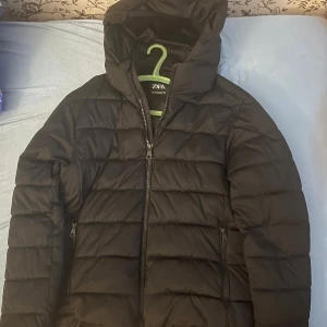 Svart pufferjacka från Zara med huva - Svart pufferjacka från Zara i storlek M. Jackan är perfekt för lite kyligare dagar. Säljer på grund att den är lite för liten för mig o då ja har köpt en ny jacka☺️jackan har bara används max 2 gånger! Skriv vid minsta fundering och pris kan diskuteras🤝