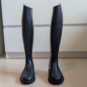 Ridstövlar från Decathlon - Säljer ett par svarta ridstövlar från Decathlon, tillverkade i syntetmaterial med textilfoder. Stövlarna har rund tå och platt sula med mönstrad undersida för extra grepp. Klassisk, hög modell som passar perfekt till ridning.