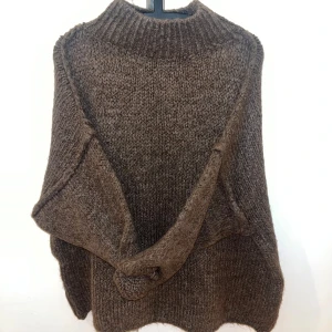 Brun oversized stickad tröja  - Supermysig brun stickad tröja från Jewelina med hög krage och oversized passform. Tröjan har långa ärmar och grovstickad struktur som ger en chill vibe. Perfekt att slänga över en skinnjacka för extra edge.