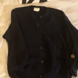 Mörkblå ullkofta med brodyr - Mysig mörkblå kofta i 100% ull med rund hals och knappar framtill. På ärmen finns en broderad detalj i rött, gult och blått. Perfekt för lager-på-lager och passar till allt. Klassisk och enkel design som funkar året om.