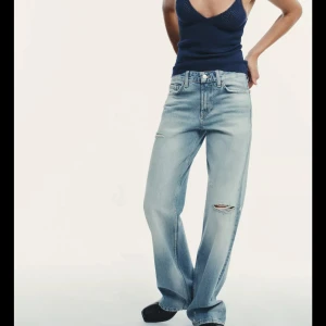 Lågmidjade Zara jeans  - Snygga ljusblå jeans med breda ben och slitna detaljer vid knä och lår från Zara. Modellen har klassisk femficksdesign och normal midja. Jeansen är tillverkade i denim och har en avslappnad, loose passform som ger en cool vibe.
