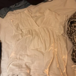 Vit blus med volang från Gina Tricot - Säljer en söt vit blus från Gina Tricot i storlek 170. Blusen har volangdetaljer vid axlarna, v-ringad hals och är tillverkad i ett lätt och luftigt material. Perfekt för dig som gillar romantisk och boho-inspirerad stil.