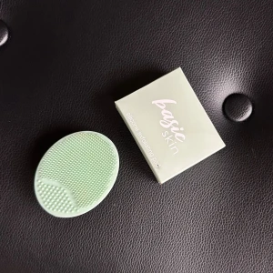 Basic Skin silikon exfolieringspad - Grön oval exfolieringspad i mjuk silikon från Basic Skin. Perfekt för att rengöra ansiktet på djupet och ta bort döda hudceller. Små och stora silikonpiggar för skonsam exfoliering. Kommer i originalförpackning, endast den ser lite tilltuftad ut, annars ny. 
