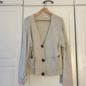 Beige stickad kofta från H&M💕💕 - Mysig beige stickad kofta från H&M med djup v-ringning och stora svarta knappar. Koftan har två praktiska fickor framtill och breda ribbade muddar vid ärmslut och nederkant. Perfekt för lager-på-lager under hösten och vintern.