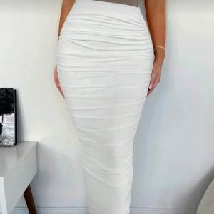 Vit långkjol med rynkade detaljer - Snygg vit långkjol med rynkade detaljer som ger en cool och modern look. Kjolen har en tight passform och är perfekt för dig som gillar stilrena och trendiga plagg. Materialet känns mjukt och följsamt mot kroppen.