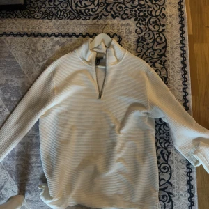 Vit ribbad half zip-tröja H&M M - Säljer en vit ribbad tröja från H&M i storlek M. Tröjan har en hög krage och half zip-dragkedja framtill. Regular fit och långa ärmar, perfekt för lager-på-lager. Materialet är mjukt och stretchigt, vilket gör den riktigt skön att bära.