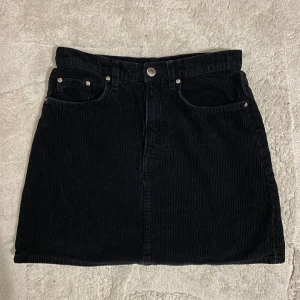 Svart manchesterkjol från Divided H&M - Svart kortkjol i manchester från Divided. Kjolen har klassisk femficksdesign, knapp och dragkedja framtill samt raka linjer. Perfekt för dig som gillar en enkel men snygg look. Tidlös modell som funkar till många stilar.