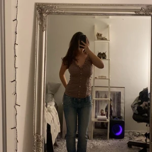 Brun korsett-topp med knappar - Säljer en brun korsett-topp med snygg v-ringning och rynkade detaljer vid bysten. Toppen har knappar hela vägen framtill och är figurnära med en feminin siluett. Perfekt att styla med jeans eller kjol för en trendig look.