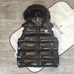 Svart dunväst från Moncler med huva - Svart, glansig dunväst från Moncler med avtagbar huva och ikonisk logga på bröstet. Västen har quiltad design, två dragkedjefickor och en innerficka med serietidningsmönster. Perfekt för att ge din outfit en cool och sportig vibe. Ingår ingår inte monkler påsen.