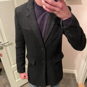 Svart kavaj från 157, storlek S - Stilren svart kavaj från 157 med klassisk passform. Kavajen har två knappar framtill, fickor med lock och slät design utan mönster. Fodrad insida för extra komfort. Perfekt för dig som vill ha en enkel och snygg look.