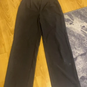 Svarta kostymbyxor från 157 XS - Snygga svarta kostymbyxor från 157 i storlek XS. Byxorna har rak passform med klassisk midja och är tillverkade i ett mjukt tyg som ger en clean look. Perfekta för dig som gillar stilrena och enkla outfits.