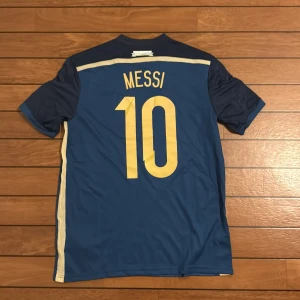 Argentina Messi VM 2014 tröja Adidas S - Säljer en officiell Argentina fotbollströja från VM-finalen 2014 med Messi och nummer 10 på ryggen. Tröjan är blå med mörkblå och ljusgula detaljer, har korta ärmar och är tillverkad i lätt, ventilerande ClimaCool-material. Adidas-logga och VM-patch på ärmarna.