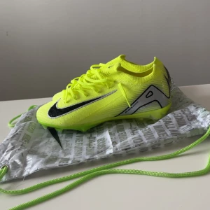 Nike Mercurial Zoom fotbollsskor gul - Nike Mercurial Zoom fotbollsskor i neon-gul med svarta detaljer och silvriga inslag. Skorna har snörning, platt sula med dobbar och är tillverkade i syntetmaterial med stickad ovandel för extra komfort och passform. Perfekta för dig som vill sticka ut på planen.