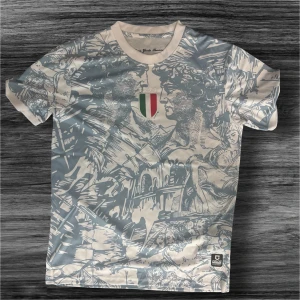 Italiensk konstinspirerad t-shirt - Snygg t-shirt från Goleador med konstnärligt tryck i blått och vitt, inspirerat av klassiska italienska motiv. På bröstet finns en patch med Italiens flagga. T-shirten har rund hals och korta ärmar, perfekt för dig som gillar unik design.