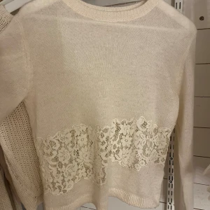 Beige stickad tröja med spets från Zara - Snygg beige stickad tröja från Zara i storlek M. Tröjan har lång ärm och ett brett band med blommig spetsdetalj över magen. Rund halsringning och mjukt material som känns skönt mot huden. Perfekt för dig som gillar romantiska detaljer.