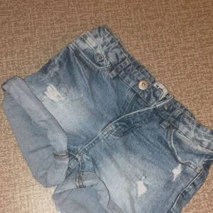 Blå jeansshorts från 157 - Snygga blå jeansshorts från 157 med slitna detaljer och upprullade benslut. Klassisk femficksmodell med knapp och dragkedja framtill samt resår i midjan bak. Perfekta för varma dagar och en avslappnad look. Pris går att diskutera!!