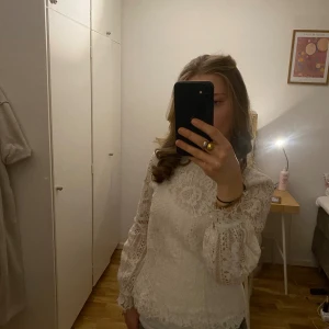 Vit spetsblus från H&M, stl 36 - Superfin vit blus från H&M i spets med långärmade puffärmar och rund halsringning. Blusen har vackra spetsdetaljer, knappar vid ärmslut och figurnära passform. Perfekt för dig som gillar romantisk och trendig stil.