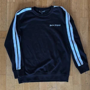 Svart Palm Angels sweatshirt  - Svart sweatshirt från Palm Angels med vita och ljusblå dubbla ränder längs ärmarna. Sällsynt tröja. Använd fåtal gånger men knappast tecken på användning. Passar både M och L. 