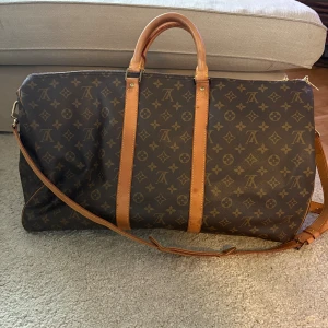 Louis Vuitton väska - Louis Vuitton resväska i klassiskt monogrammönster med bruna och beige detaljer. Väskan har både handtag och axelrem i skinn, samt dragkedja upptill. Perfekt storlek för weekendresor och har den ikoniska LV-loggan över hela väskan. Storlek 55