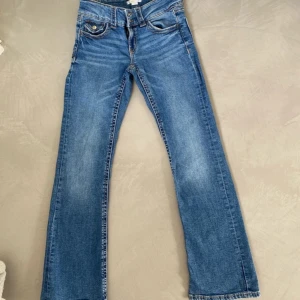 Blå bootcut jeans från Gina Tricot  - Snygga blå jeans från Gina Tricot med bootcut-ben och klassisk femficksdesign. Jeansen har dubbla knappar i midjan och är tillverkade i mjukt denimtyg med lätt slitning. Perfekt passform och coola detaljer vid fickorna.