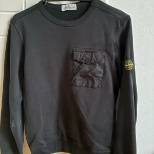 Svart Stone Island sweatshirt junior - Svart sweatshirt från Stone Island med en liten ficka vid bröstet och såklart märket på armen. Tröjan är 100% äkta 