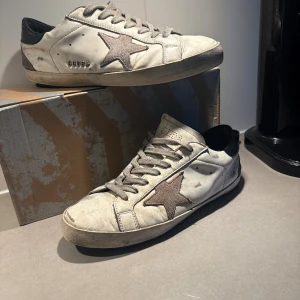 Golden Goose sneakers med stjärna - Snygga sneakers från Golden Goose i vitt skinn med grå snörning och en grå stjärna på sidan. Skorna har svart hälparti och klassisk låg profil. Perfekta för dig som gillar en avslappnad och trendig stil.