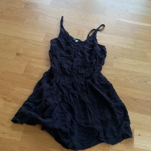 Svart kort playsuit med smala axelband - Svart kort playsuit med smala axelband och v-ringning. Modellen är ärmlös och har en markerad midja. 