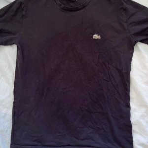 Svart t-shirt från Lacoste i bomull - Snygg svart t-shirt från Lacoste med klassisk krokodillogga broderad på bröstet. T-shirten är i mjuk bomull och har en enkel, stilren design med rund hals och korta ärmar. Perfekt för en clean och avslappnad look.