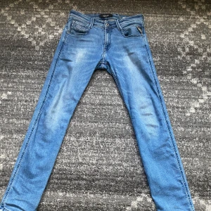 Replay Anbass ljusblå jeans 29/32 - Säljer ett par Replay Anbass jeans i ljusblå tvätt med klassisk femficksdesign och snygga slitningar. Jeansen har smal passform och raka ben, perfekt för dig som gillar en modern look. Materialet är mjukt och stretchigt jeans för extra komfort.