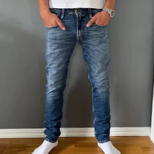 Replay Anbass slim fit jeans blå - Säljer ett par Replay Anbass slim fit jeans i klassisk blå tvätt. Jeansen har fem fickor, snygga slitningar och Replay-logga på bakfickan. De är tillverkade i stretchig denim för en bekväm passform och har smalare ben. Perfekta för dig som gillar en modern och stilren look.
