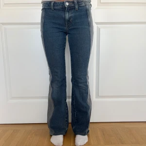 Bootcut jeans från Weekday, blå/grå - Bootcut jeans från Weekday i blå denim med grå paneler längs sidorna. Låg midja och klassisk femficksmodell. Jeansen har en snygg kontrast mellan blått och grått tyg och råa kanter nertill. Perfekta för dig som gillar en unik twist på klassiska jeans. Passar perfekt om du är 160cm eller kortare💕💕