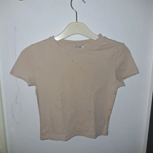 Beige croppad t-shirt - En basic beige croppad t-shirt från H&M Divided. Modellen har rund halsringning och korta ärmar. Tillverkad i mjuk bomull, perfekt för en enkel och clean look. Passformen är normal och toppen är lätt att matcha med allt. Har fläckar på två ställen, därför kan den skickas med gratis vid köp av något annat😊