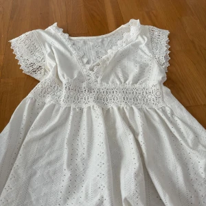 Vit spetströja från SHEIN S - Superfin vit kortklänning från SHEIN i storlek S. Klänningen har v-ringning, spetsdetaljer vid midjan och ärmarna samt broderat mönster över hela tyget. Perfekt för sommarens alla tillfällen och ger en romantisk vibe.