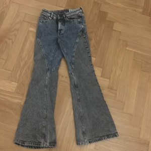 Grå bootcut jeans med coola sömmar - Säljer ett par grå jeans med unika, markerade sömmar och breda bootcut-ben. Jeansen har en snygg tvättad look och klassisk femficksdesign. Perfekta för dig som vill sticka ut med en retro vibe.