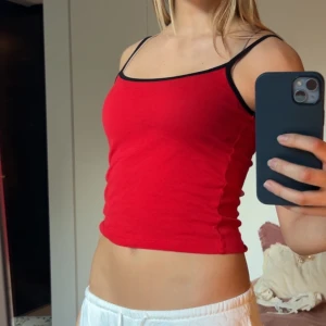 Röd linnetopp från Iets Frans - Säljer en röd linnetopp från Iets Frans med tunna svarta axelband och svarta kanter. Materialet är mjukt och stretchigt, troligtvis bomull eller polyester. Aldrig använd 