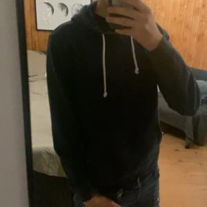 Mörkblå hoodie från Pier One - Säljer en stilren mörkblå hoodie från Pier One med vita snören och klassisk huva. Tröjan har en känguruficka framtill och är tillverkad i mjuk bomullsmix. Perfekt för chill dagar eller när du vill ha en enkel och snygg look.