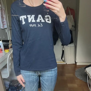 Mörkblå långärmad tröja från GANT - Snygg mörkblå långärmad tröja från GANT med vit logga och texten 'Est. 1949' framtill. Tröjan har rund halsringning och är gjord i mjuk bomull, perfekt för en chill och stilren look.