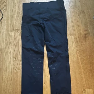 Mörkblå ridbyxor från Horse Life - Snygga mörkblå ridbyxor från Horse Life med hög midja och elastisk linning. Byxorna är halvskodda för extra fäste i sadeln och diskret logga på höften. Perfekta för dig som vill ha både stil och funktion i stallet. Aldrig använda pågrund av att de var för långa 