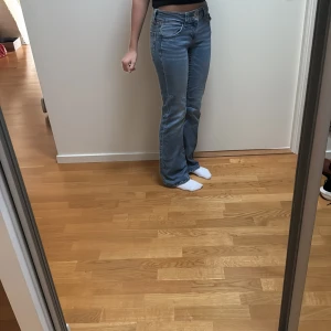 Blå bootcut jeans från Gina Tricot - Snygga blå jeans från Gina Tricot i bootcut-modell med klassisk femficksdesign och dubbla silverknappar i midjan. Jeansen är bootcut och lågmidjade. Jeansen är tillverkade i mjukt denimtyg som sitter skönt hela dagen.