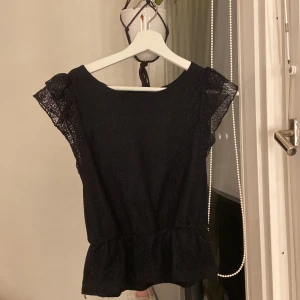 Svart spetsblus från BikBok - Supersöt svart blus från BikBok i storlek S. Blusen har korta ärmar i spets, volang nertill och ett vackert spetsmönster över hela plagget. Perfekt för dig som gillar romantiska detaljer och vill ha en feminin look.