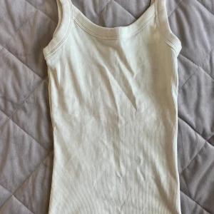 Ribbad vit linnetopp från Gina Tricot - Säljer en enkel och stilren ribbad vit linnetopp från Gina Tricot. Toppen har breda axelband och är tillverkad i mjuk bomull med stretch. Perfekt att matcha med jeans eller kjol för en clean look.