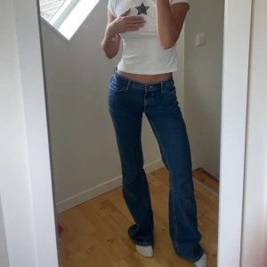 Blå bootcut jeans med låg midja - Säljer ett par klassiska blå jeans med bootcut och låg midja. Jeansen har fem fickor, bälteshällor och stängs med knapp och dragkedja. Perfekt passform och snyggt fall över. 